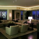 Linear ceiling lighting wraps around a living room overlooking a city landscape.
