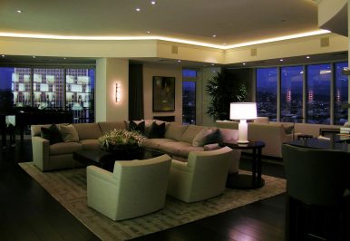 Linear ceiling lighting wraps around a living room overlooking a city landscape.