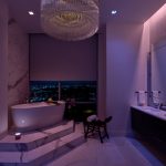 A bathroom with a soaking tub illuminated in a violet hue. Lutron’s shades are partially lowered over the windows.