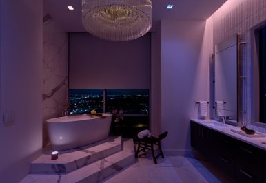 A bathroom with a soaking tub illuminated in a violet hue. Lutron’s shades are partially lowered over the windows.